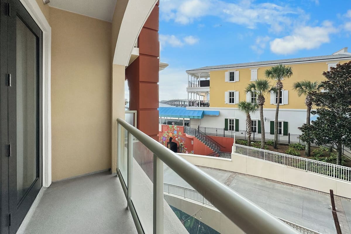 A balcony with a clear view of a yellow building, palm trees, and a blue awning.