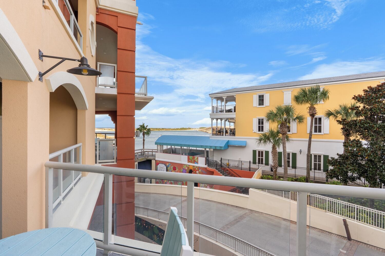 Un balcon donnant sur une zone riveraine, avec notamment un bâtiment doté d’un auvent bleu et de palmiers.