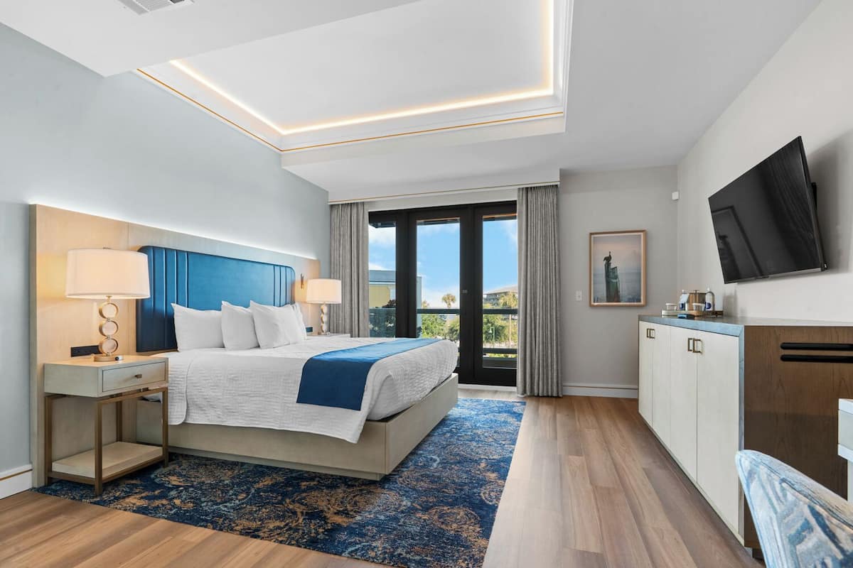 A hotel room with a bed, bedside tables, a TV, a desk, and a view of the outdoors.
