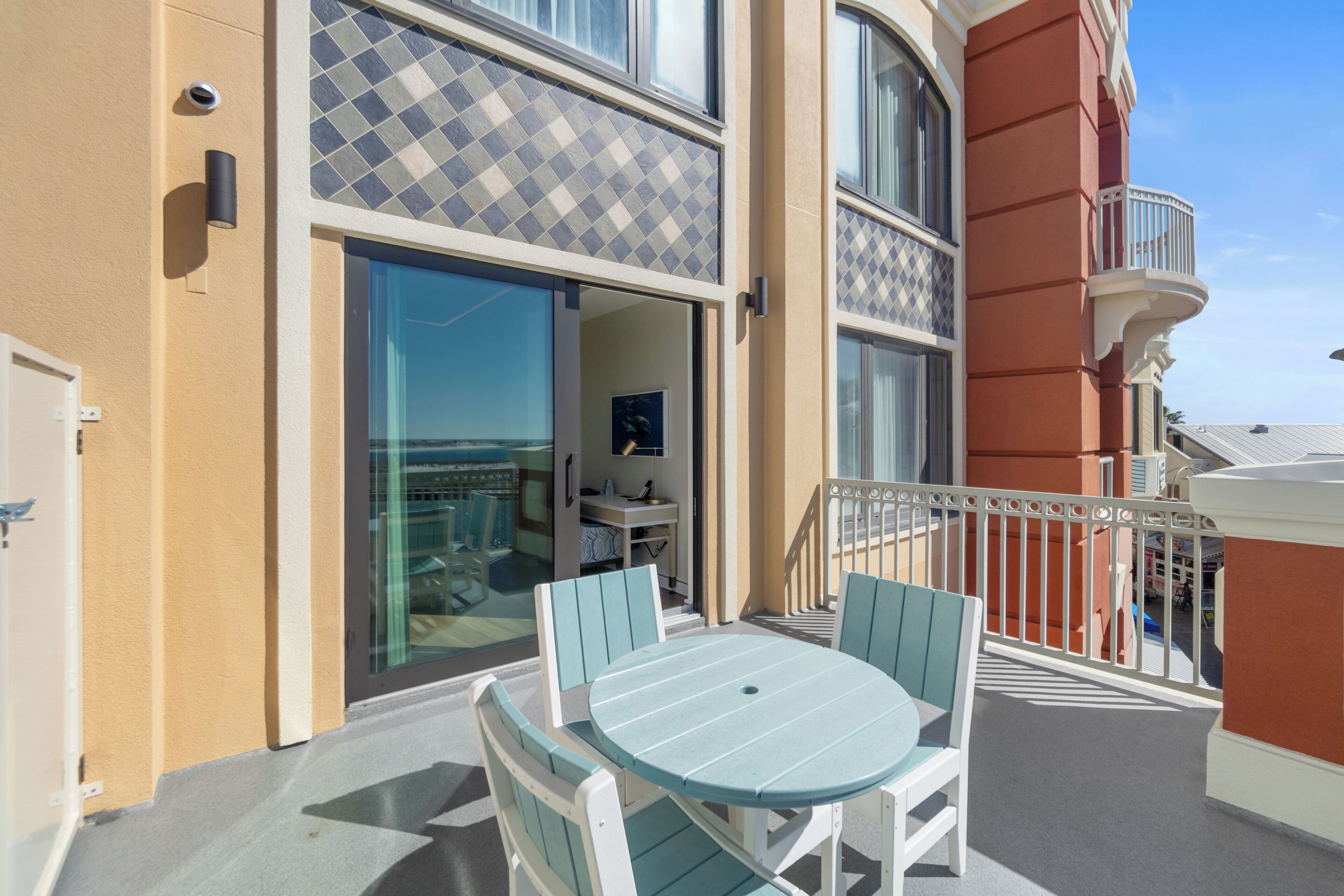 Un balcon avec une table et des chaises, une porte vitrée donnant sur un espace intérieur et un mur orné de motifs.