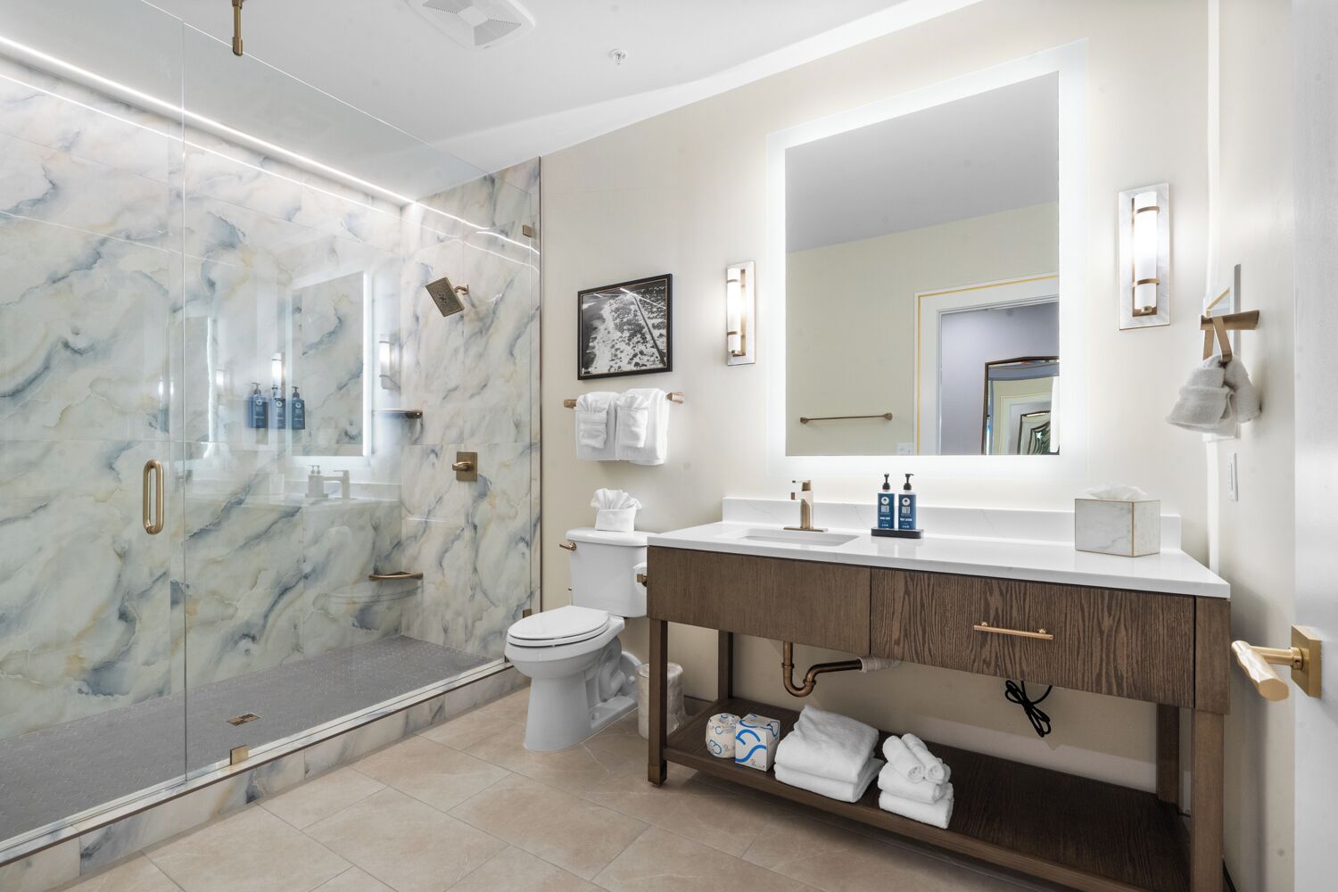 A modern bathroom with a glass shower enclosure, a toilet, a vanity with a mirror, and a shelf with towels.