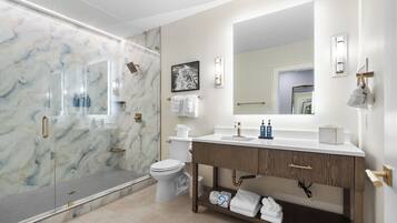 A modern bathroom with a glass shower enclosure, a toilet, a vanity with a mirror, and a shelf with towels.