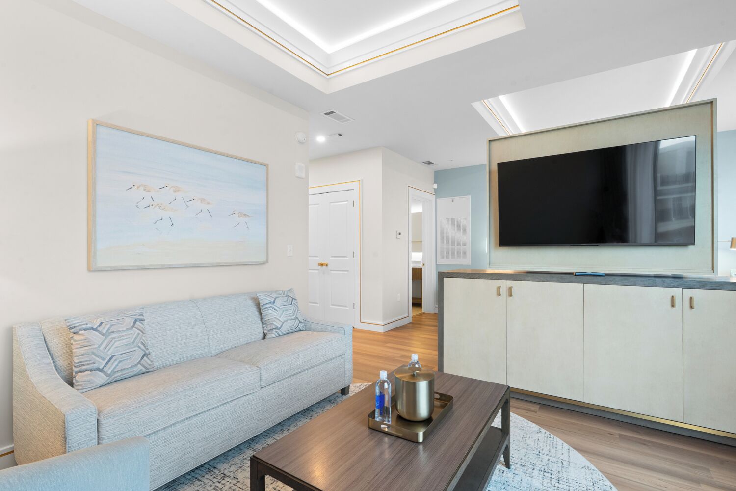 Una sala de estar moderna con un sofá, una mesa de centro con botellas, un cuadro y un televisor montado en la pared.