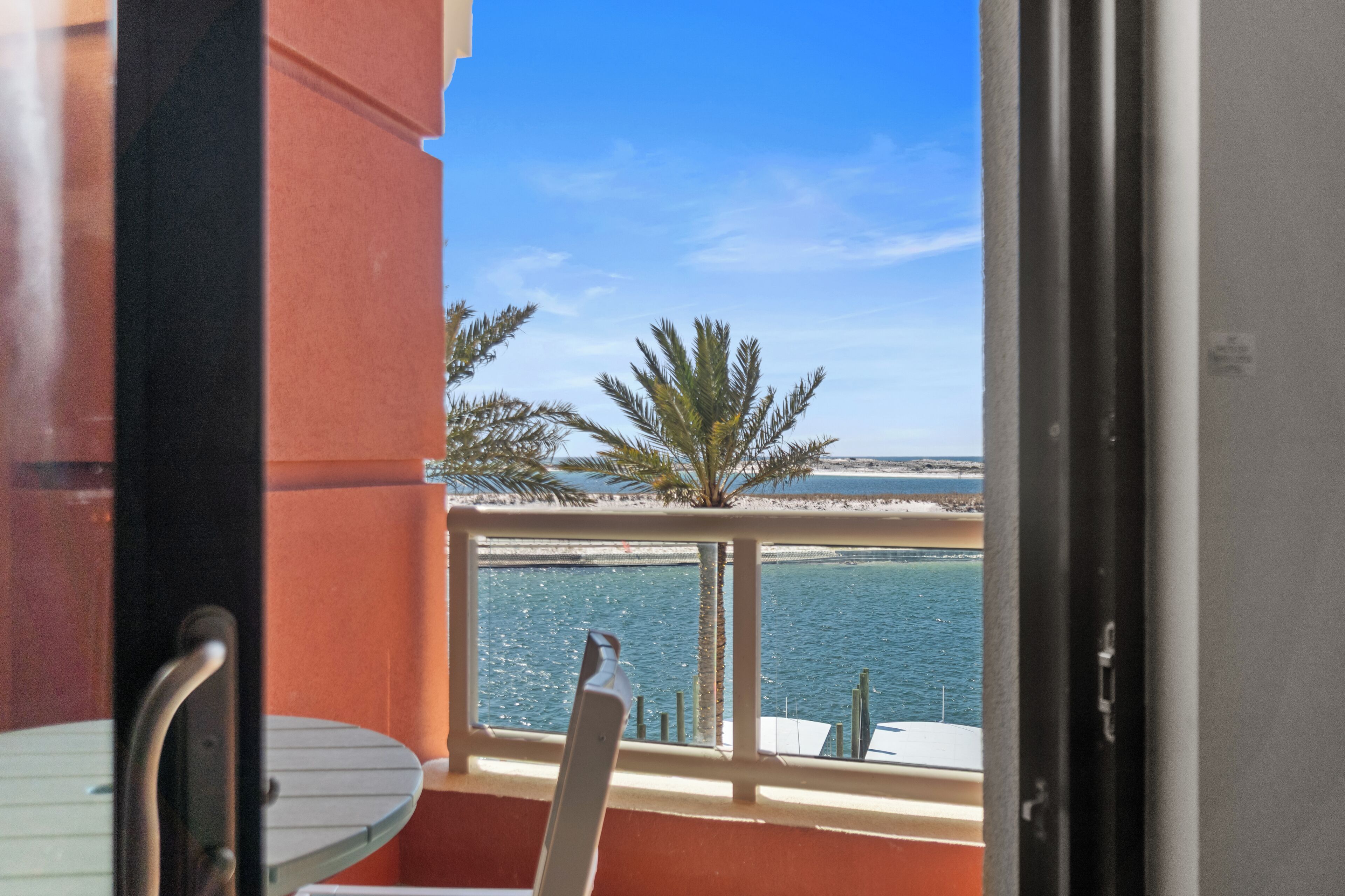 A balcony with a view of the sea, a palm tree, and a chair.