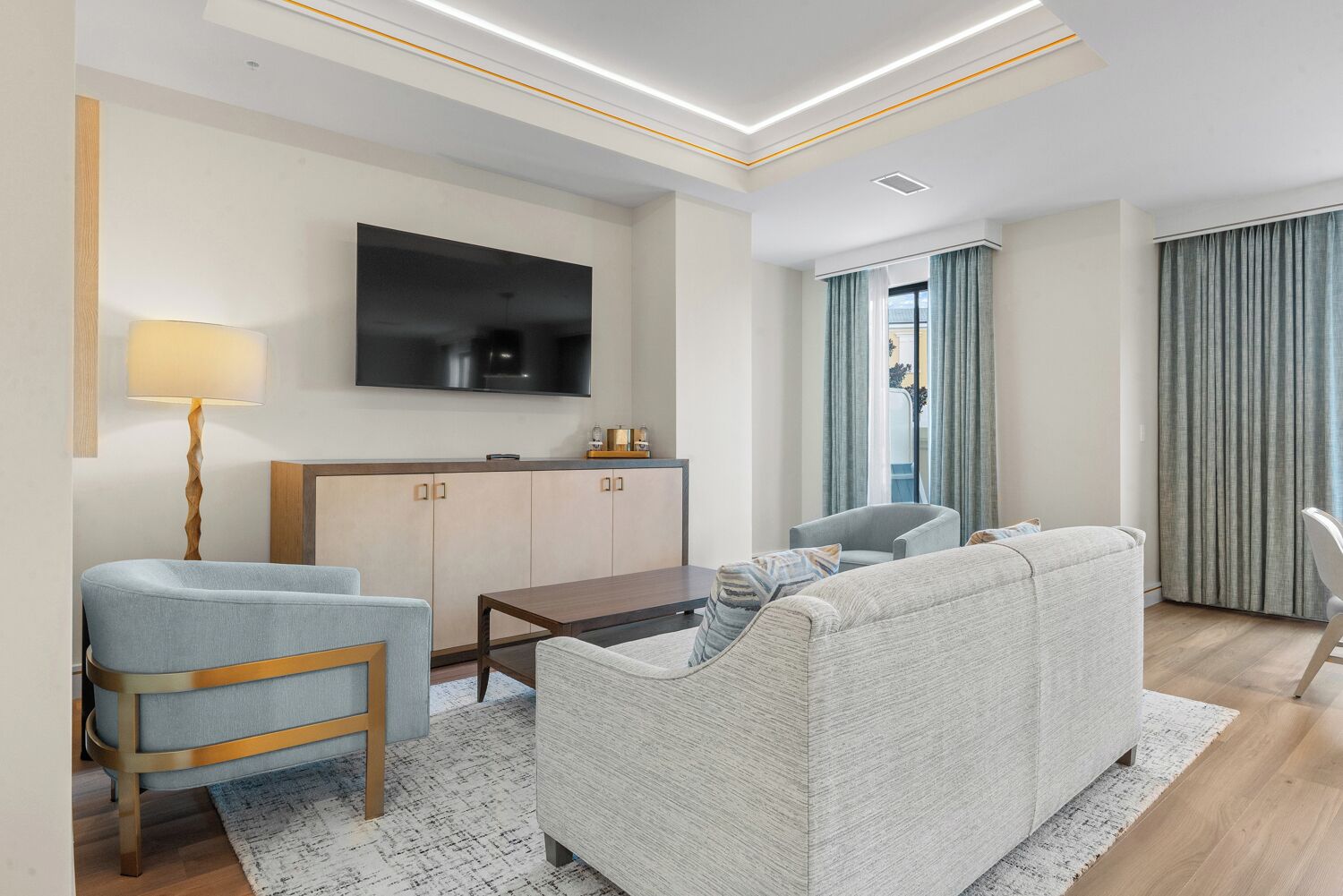 Een moderne woonkamer met een bank, fauteuils, een salontafel, een flatscreen televisie en een houten kast.