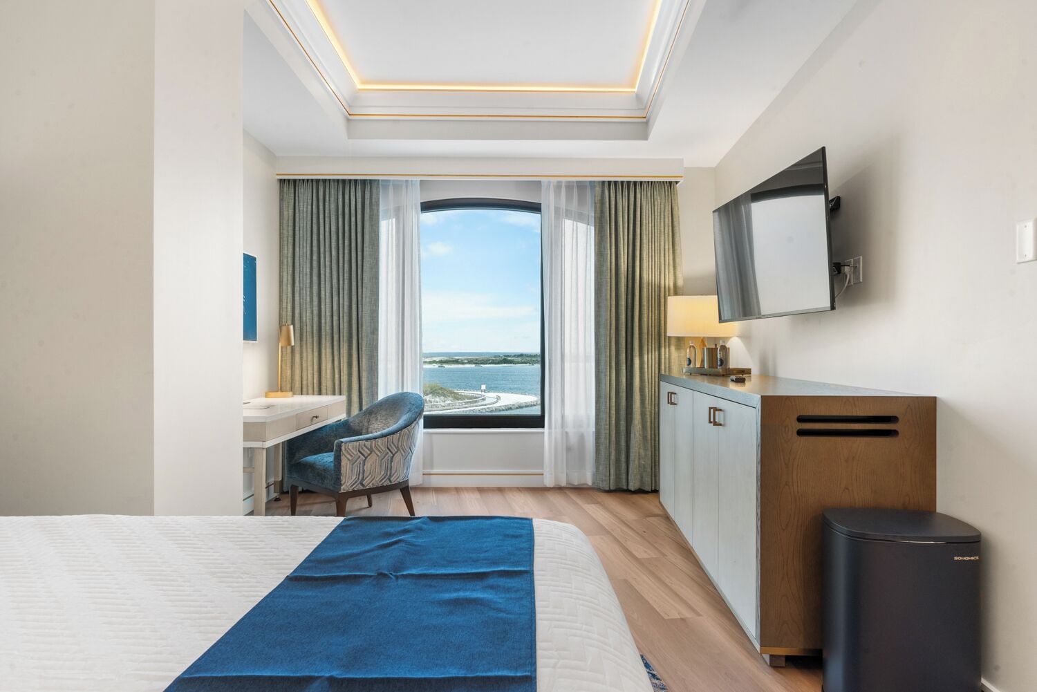 Une chambre d’hôtel avec un grand lit, un bureau, une chaise, une télévision et une vue sur la mer.