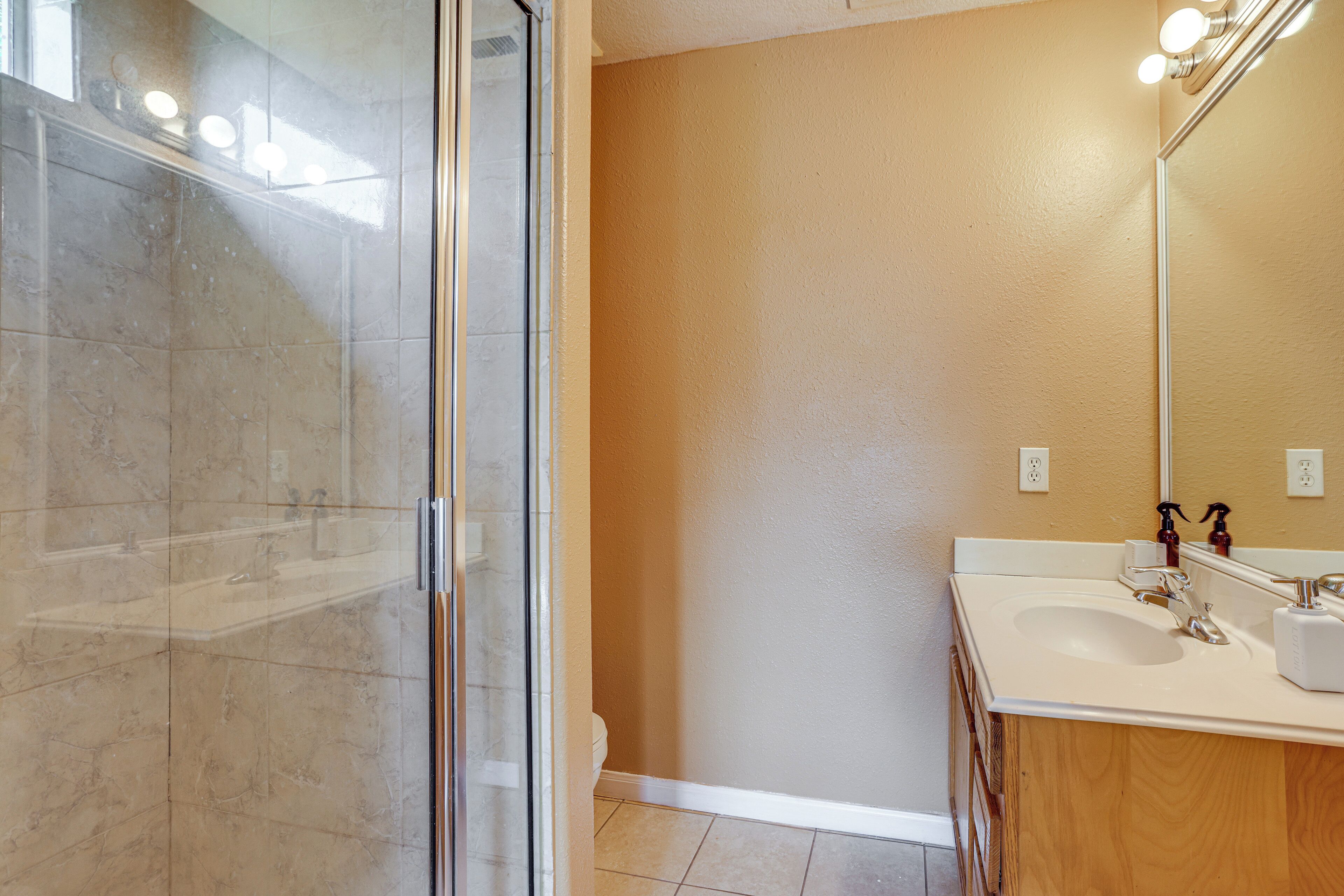 A bathroom with a glass shower enclosure, a sink, a mirror, and a wooden vanity.