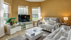 Ein Wohnzimmer mit Flachbildfernseher, einer Couch, einem Couchtisch und einem TV-Schrank mit einer Pflanze.