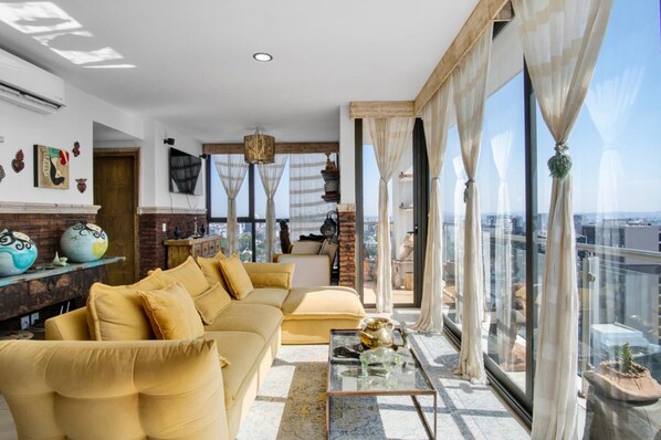 Una sala moderna con un sofá, una mesa de centro y ventanas grandes que dan a una vista de la ciudad.