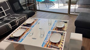 Ein modernes Wohnzimmer mit Esstisch für vier Personen, einer Couch und Blick auf eine Terrasse mit Sitzgelegenheiten.