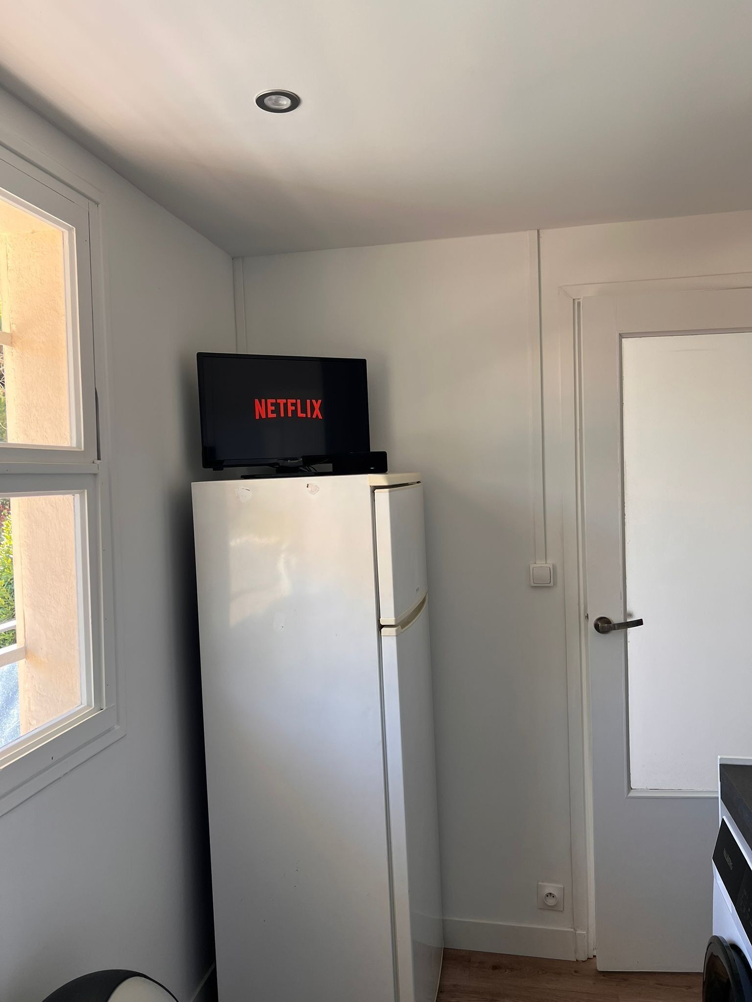 Ein Zimmer mit einem weißen Kühlschrank, einer Tür und einem Fenster.