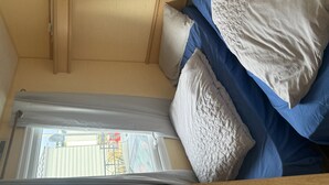 A compact RV interior with a bed, pillows, and a window providing a view of the outside. - Chapel Saint Leonards - Happy Days Sleeps 6 (Skegness)