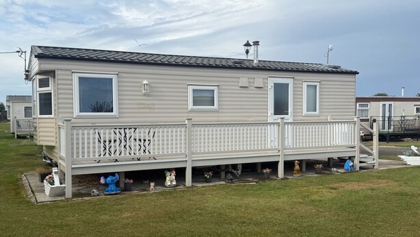 A mobile home with a fenced deck, multiple windows, and a chimney. - Chapel Saint Leonards - Happy Days Sleeps 6 (Skegness)