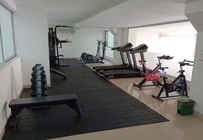 Un gimnasio con cintas de correr, una bicicleta estática y una banca.