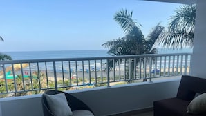 A balcony with a view of the beach, a wicker chair, a sofa, and a small round table.