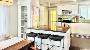 Uma cozinha moderna com uma ilha central, banquetas, uma mesa de jantar e uma luminária pendente.