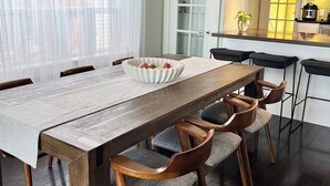 Uma sala de jantar com uma mesa de madeira, seis cadeiras, uma tigela branca com frutas e um candelabro.