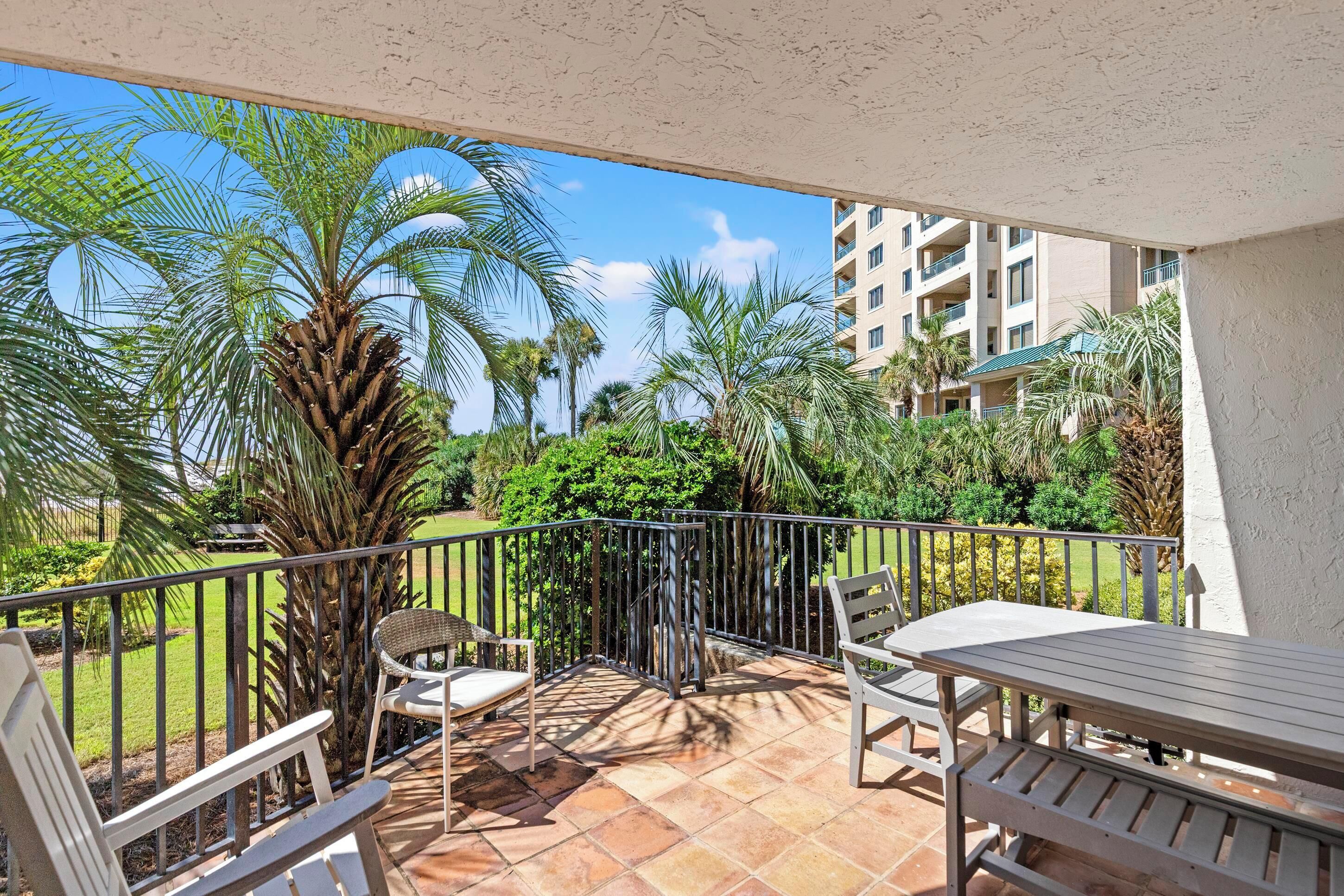 Un balcon avec une table et des chaises, entouré de palmiers et offrant une vue sur un immeuble.