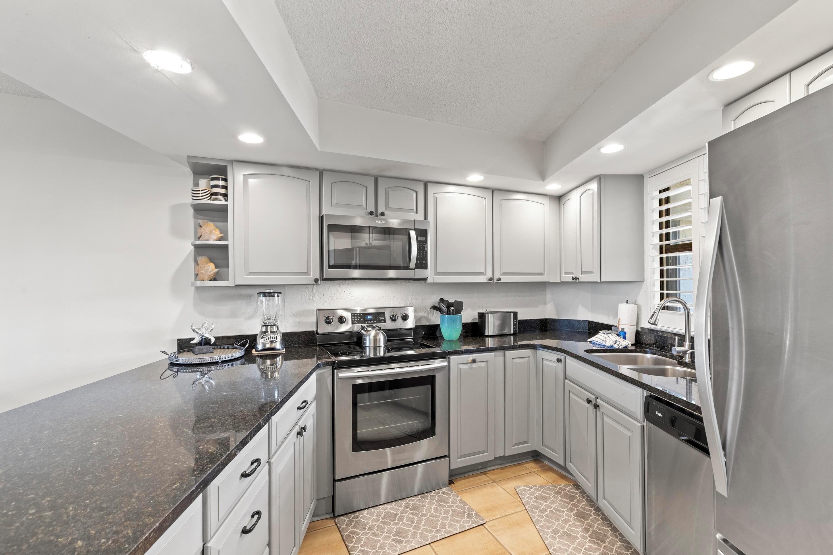 A modern kitchen with grey cabinets, stainless steel appliances, and a granite countertop.