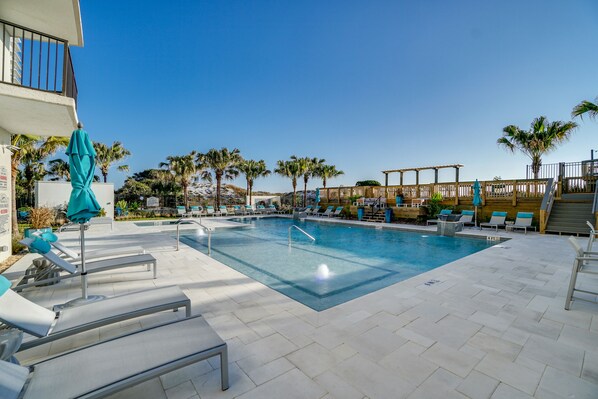 A pool area with lounge chairs and umbrellas, surrounded by palm trees and a wooden deck. - Beachside One at Sandestin by PHG (Miramar Beach)
