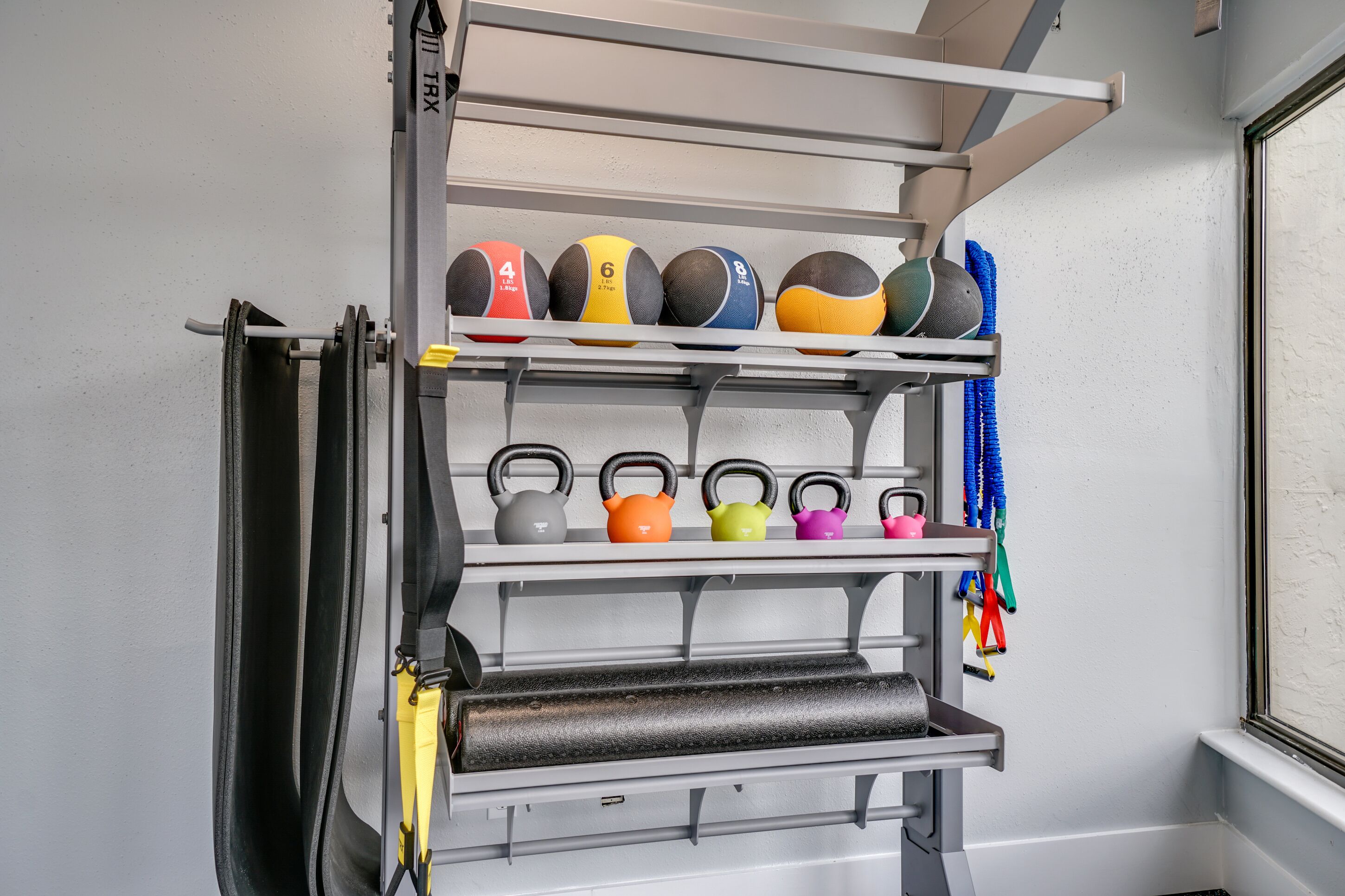 A wall-mounted rack with various exercise equipment, including kettlebells and resistance bands.