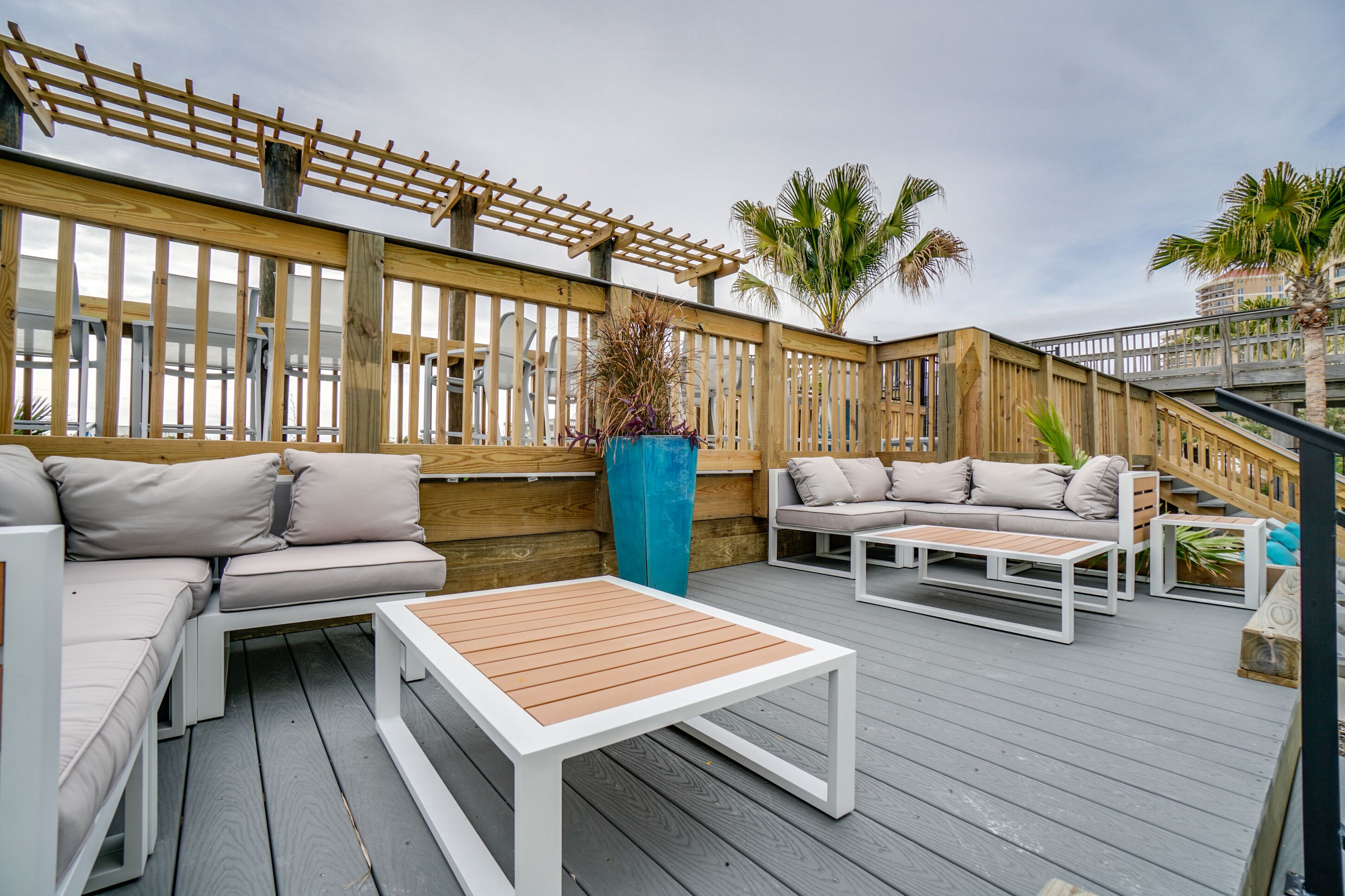 Eine Terrasse im Freien mit Holzboden, einer Holz-Pergola und zwei weißen Sofas mit beige farbenen Kissen.