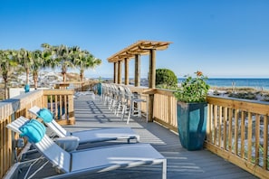 A wooden deck with lounge chairs and a pergola overlooking a beach.