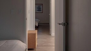 Un couloir étroit, avec un lit sur la gauche et une commode en osier au centre.