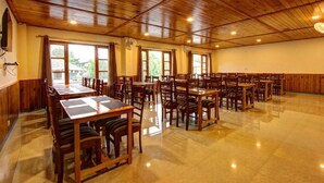 A spacious indoor dining area with wooden tables and chairs, large windows, and a polished floor. - Luxe Signature  (Manali)