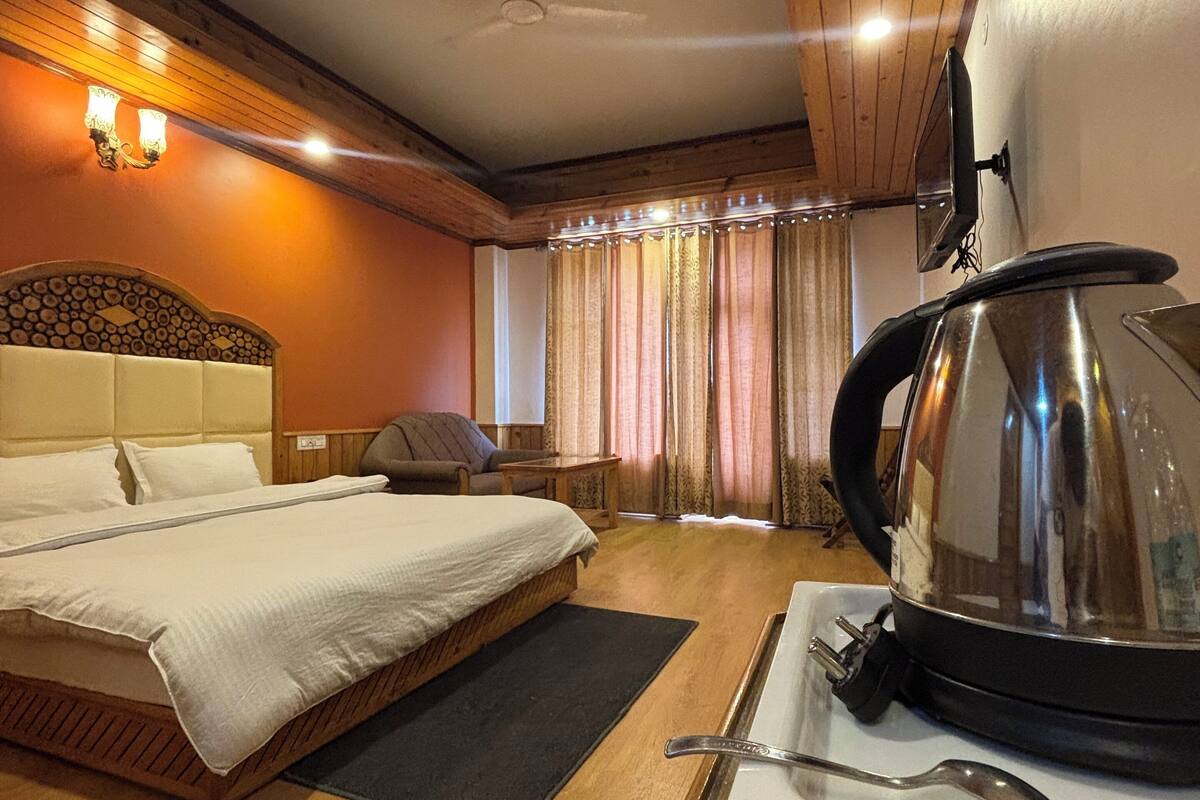 A hotel room with a wooden bed, a large kettle, and a TV on the wall.