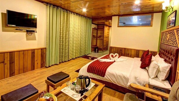 A wooden-paneled room with a bed, a TV, a table with a kettle, and a window with curtains. - Luxe Signature  (Manali)