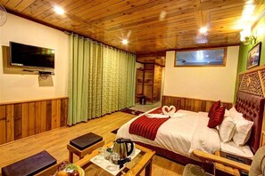 A wooden-paneled room with a bed, a TV, a table with a kettle, and a window with curtains. - Luxe Signature  (Manali)