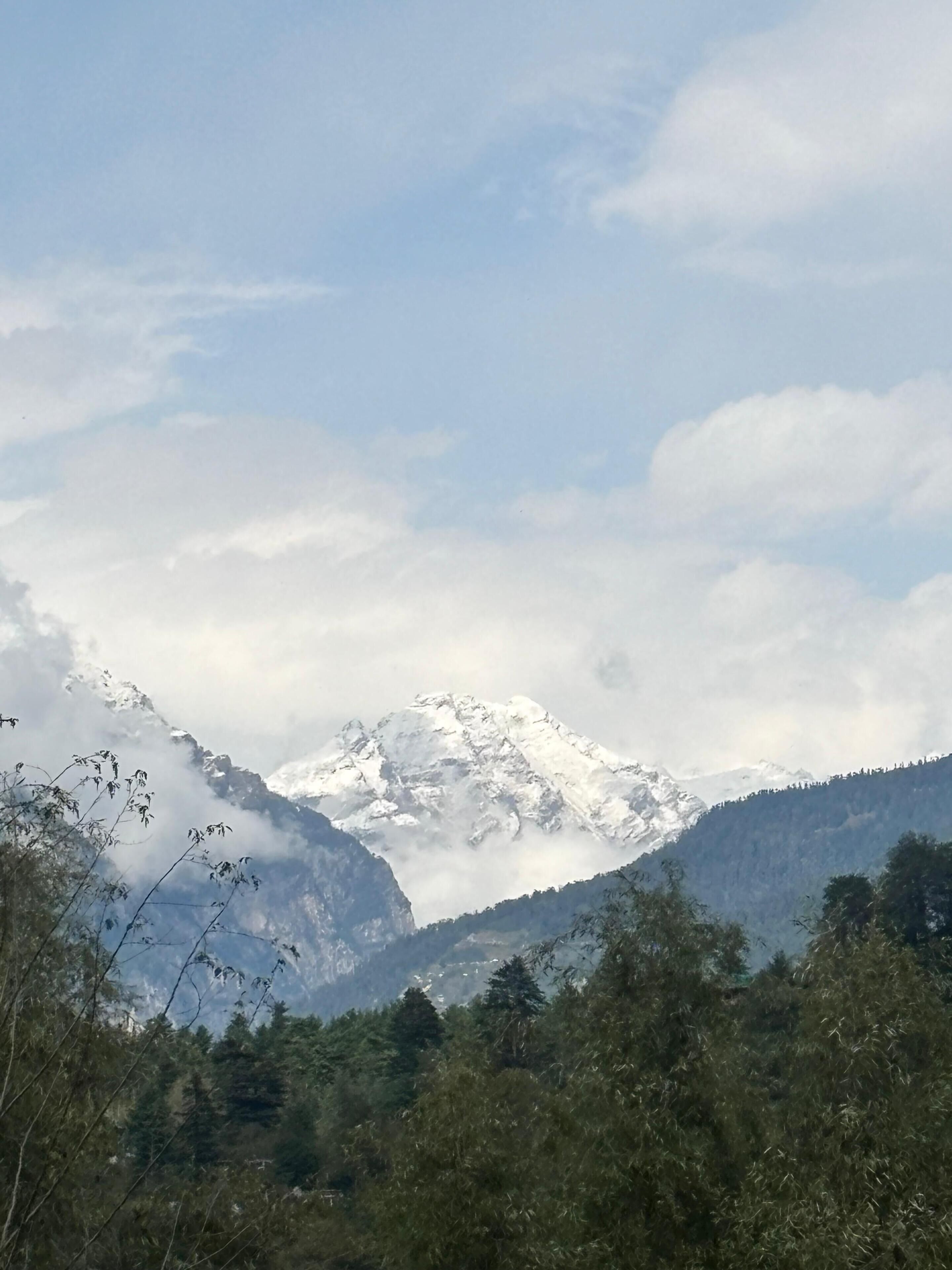 A mountain landscape with snow-capped peaks, forested valleys, and a clear sky.