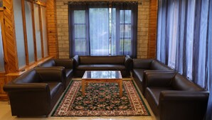A living room with a brown leather sofa set, a glass coffee table, and a patterned rug. - Luxe Signature  (Manali)