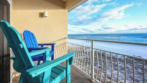 Ein Balkon mit zwei türkisblauen Adirondack-Stühlen, einem kleinen Tisch und Blick auf Strand und Meer.