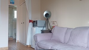 Een woonkamer met een bank, een glazen salontafel, een klok aan de muur en een keuken in de achtergrond.