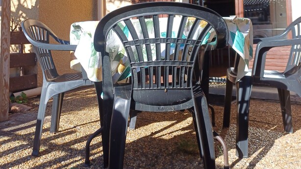 Een buitenruimte met twee stoelen en een tafel, een houten pergola en een toegang tot een gebouw.