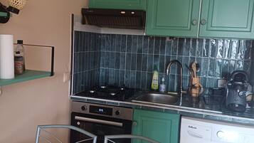 Une cuisine de taille réduite avec des meubles de couleur verte, une cuisinière, un four et un lave-linge.