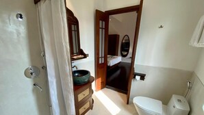 A compact bathroom with a toilet, a sink with a bowl, a mirror, and a shower area. - Tranquil Truc Bach (Hanoi)