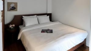 A bedroom with a wooden bed, white bedding, a nightstand with a vase, and a wall-mounted artwork. - Tranquil Truc Bach (Hanoi)