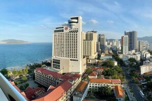 A coastal cityscape with a prominent hotel featuring a red and white facade, surrounded by other buildings and a view of the sea. - MASTER Gold Coast Ocean View (Nha Trang)