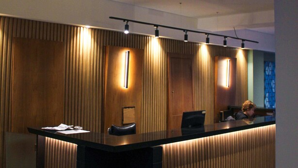 Una recepción con diseño moderno, que cuenta con un panel de madera en el fondo y una barra en color negro.