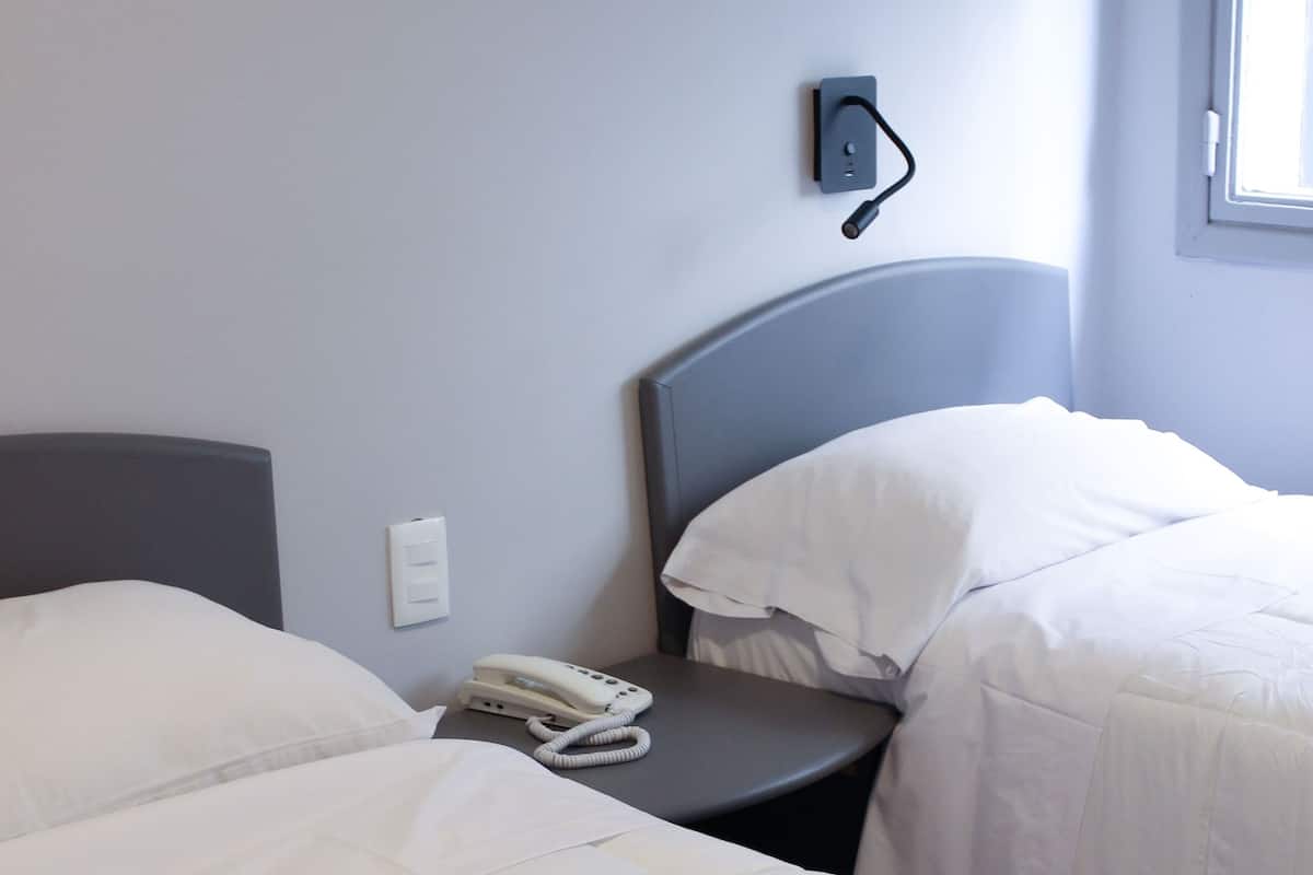 A hotel room with two beds, a bedside telephone, and a window with blinds.