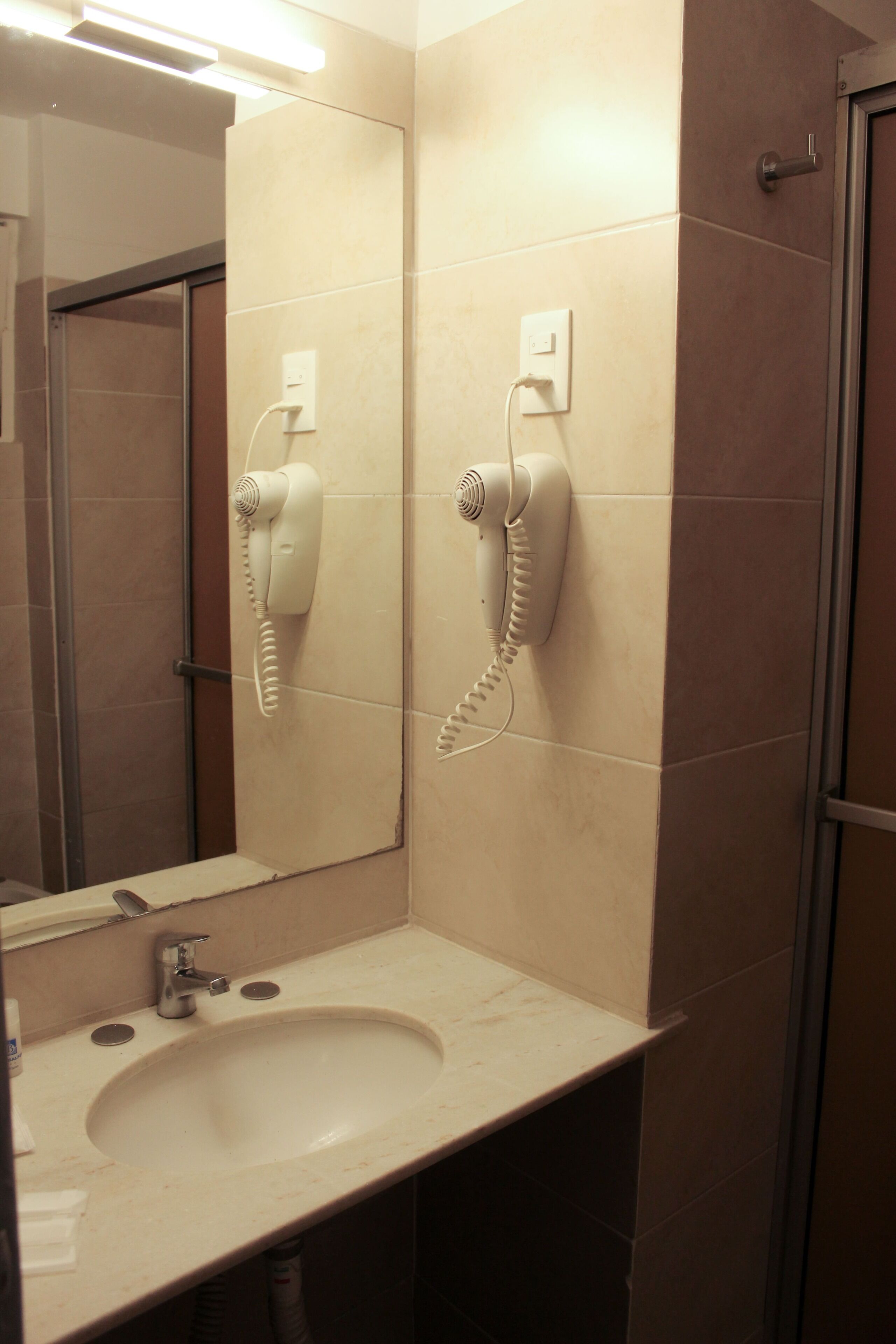 Een badkamer met een wastafel, spiegel en twee haardrogerhouders aan de muur.