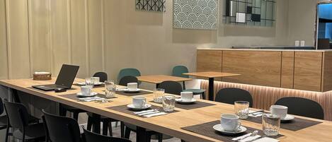 A modern dining area with a long wooden table, black chairs, and green pendant lights.