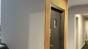 Un pasillo con puerta de madera, una escalera y piso alfombrado.