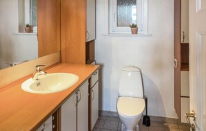 Une petite salle de bain avec un meuble-lavabo en bois, un lavabo blanc, des toilettes et une fenêtre donnant sur des arbres.
