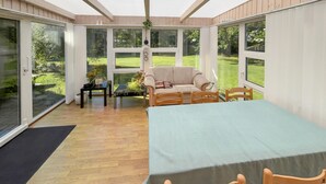 A sunroom with a dining table, chairs, a sofa, and large windows offering a view of a garden. - 3 bedroom gorgeous home in Ulfborg (Ulfborg)