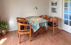 Un coin repas avec une table et des chaises en bois, une nappe à motifs, une suspension et des tableaux encadrés accrochés au mur.