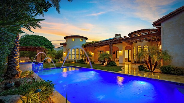 Una piscina con fuente, rodeada de abundante vegetación y un patio bien iluminado.